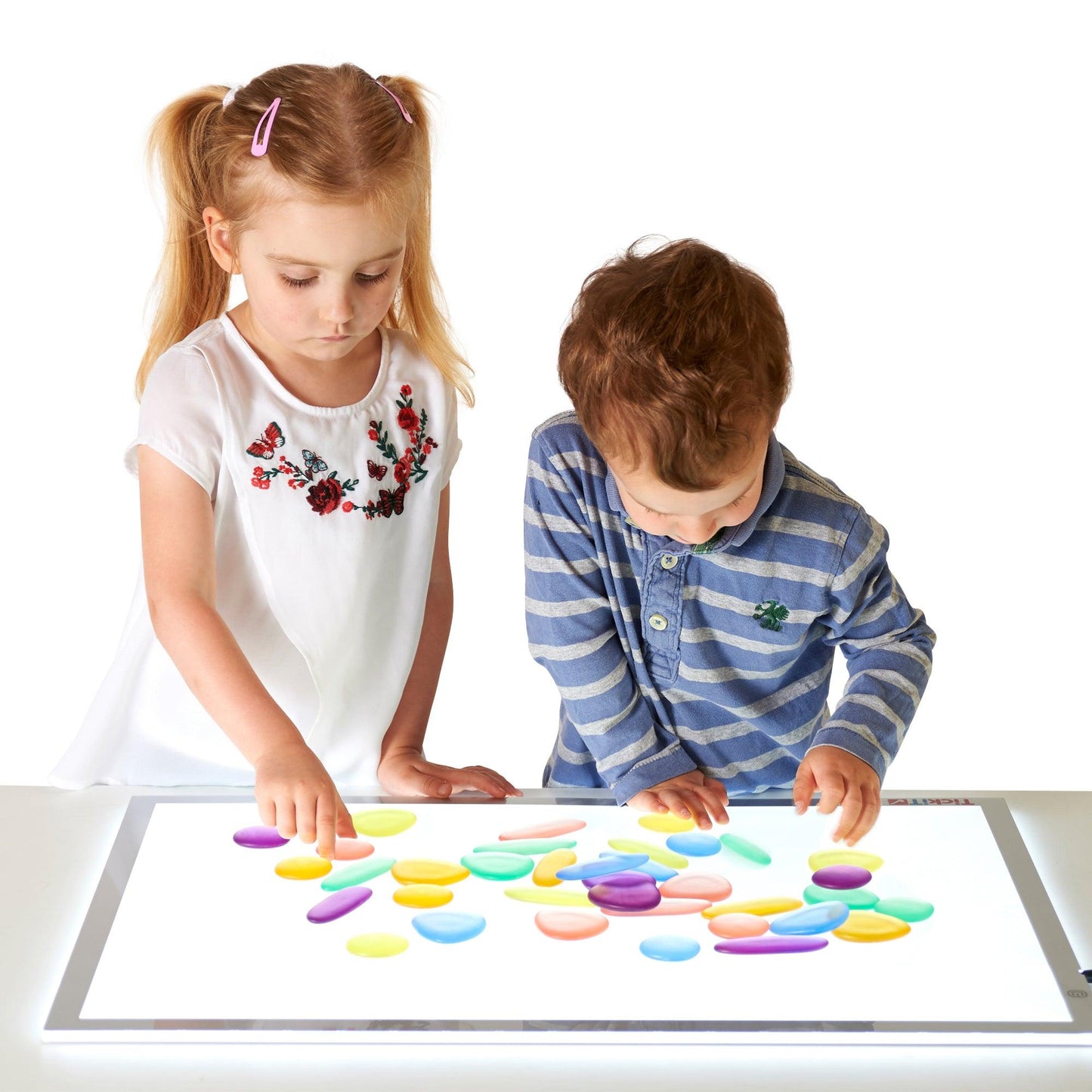 Two young children playing with colourful Rainbow Pebbles on the floor, engaging in play-based learning activities inspired by storytelling.