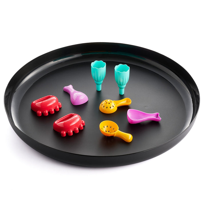A black sensory play tray with colorful tactile scoops and massage tools, including red, yellow, purple, and turquoise implements arranged in a circular layout.